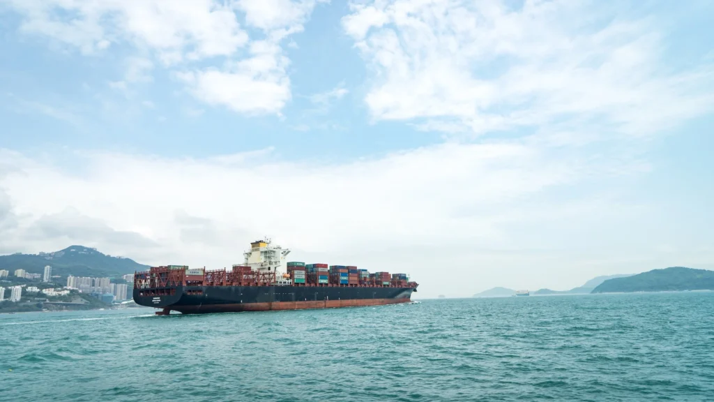 large shipping boat at sea with city coast in the back