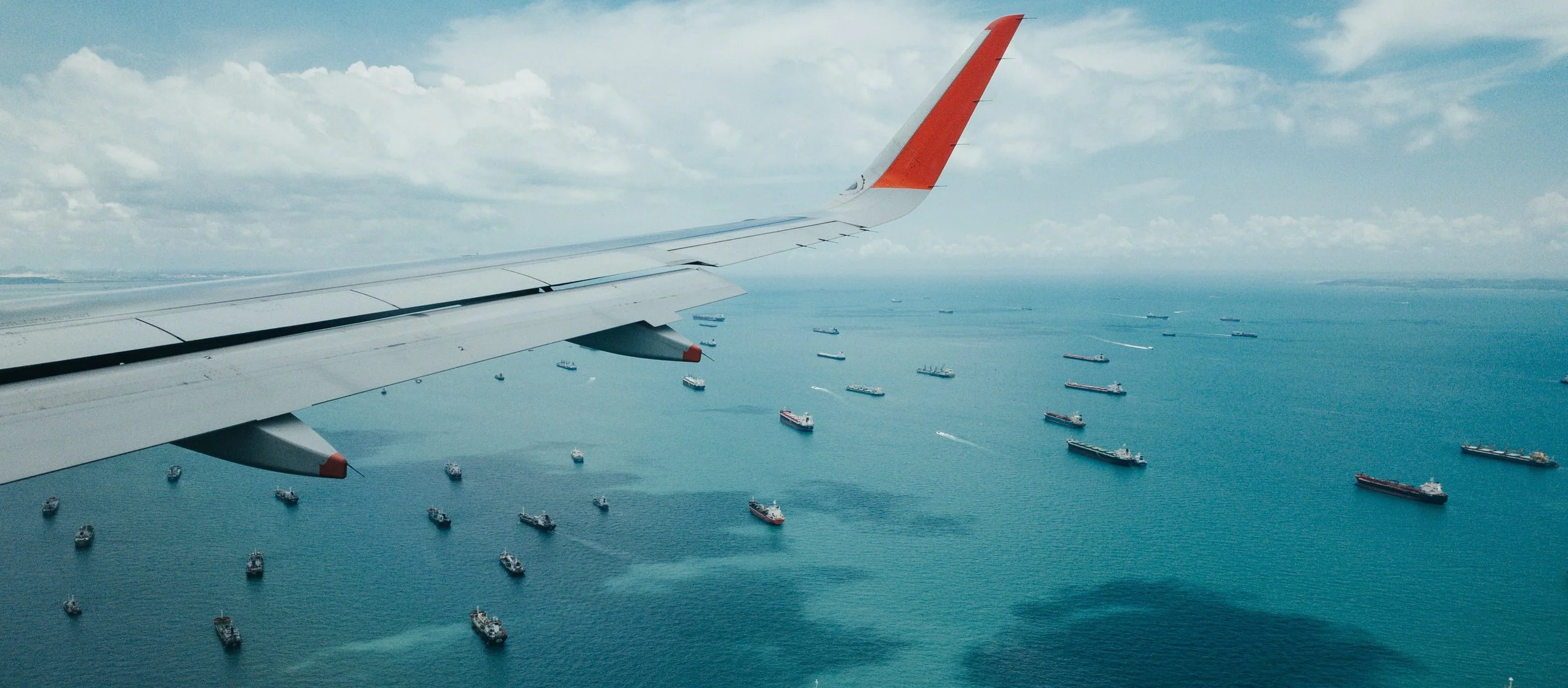 View of airplane wing with sea and boats below View of airplane wing with sea and boats below