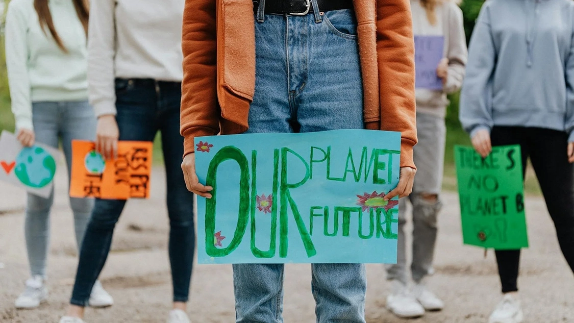 Image of women holding banners at protest at knee height. Banner reads: Our Planet, Our Future. Image of women holding banners at protest at knee height. Banner reads: Our Planet, Our Future.