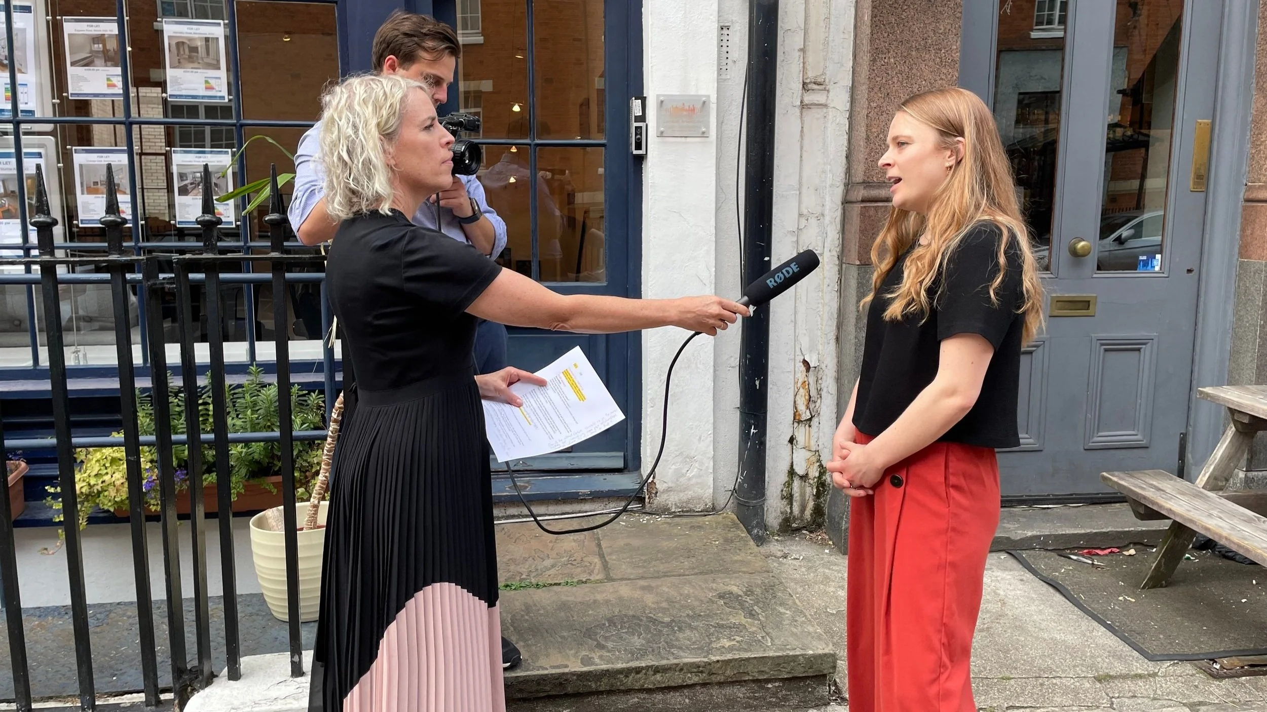 One women holds microphone and interviews another woman, standing on the street One women holds microphone and interviews another woman, standing on the street