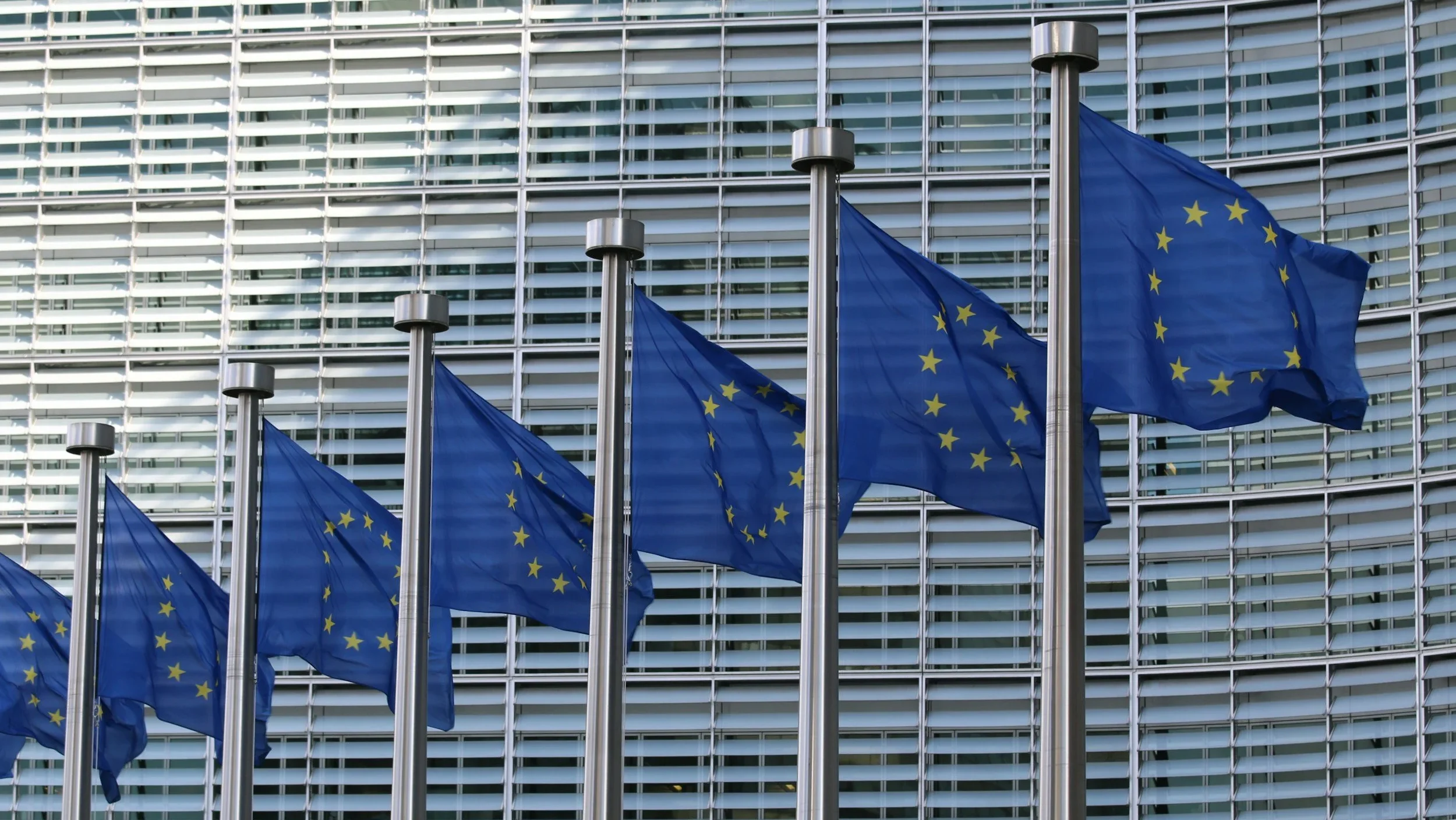 photo of a row of 7 EU flags in front of official building of the EU Commission photo of a row of 7 EU flags in front of official building of the EU Commission