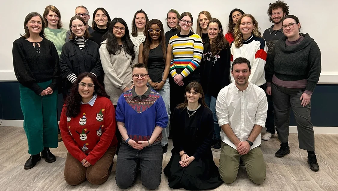 20 people pose for a photo smiling. They are in three rows. Some wear Christmas jumpers. 20 people pose for a photo smiling. They are in three rows. Some wear Christmas jumpers.