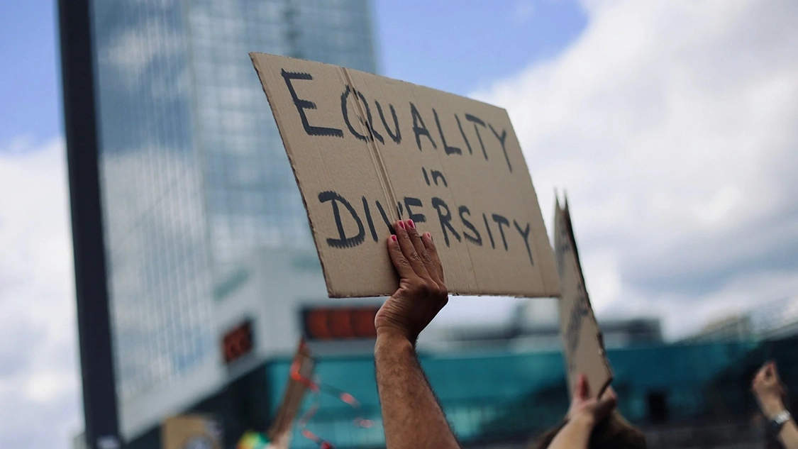 Photo of someone holding a banner made of brown cardboard with "Equality and Diversity" written on it.