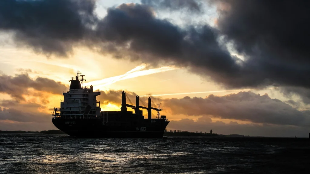 photo of shipping ship sailing into the open sea with sunset in the back